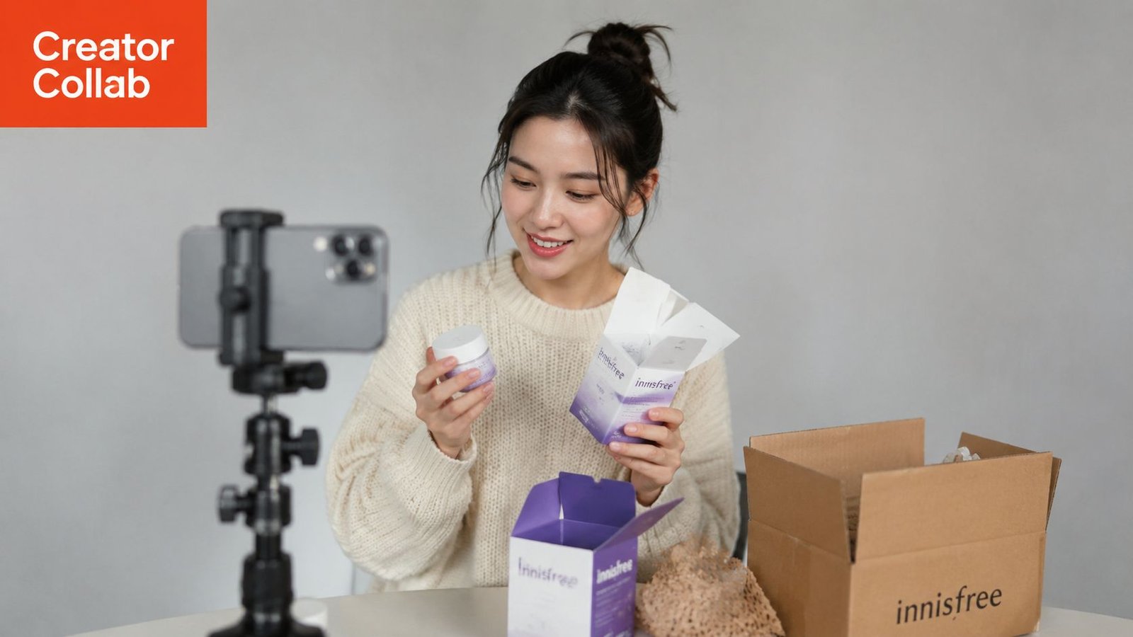 A smiling young woman records a product review video for Innisfree skincare while sitting at a desk.