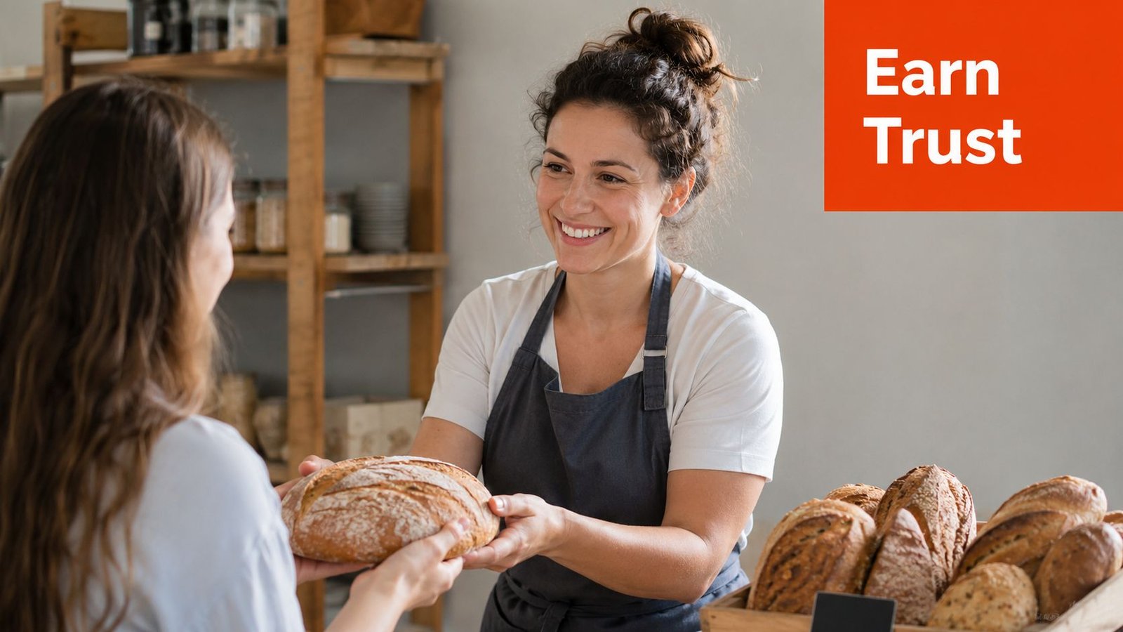 A friendly baker in an apron smiles while handing a loaf of fresh bread to a customer.